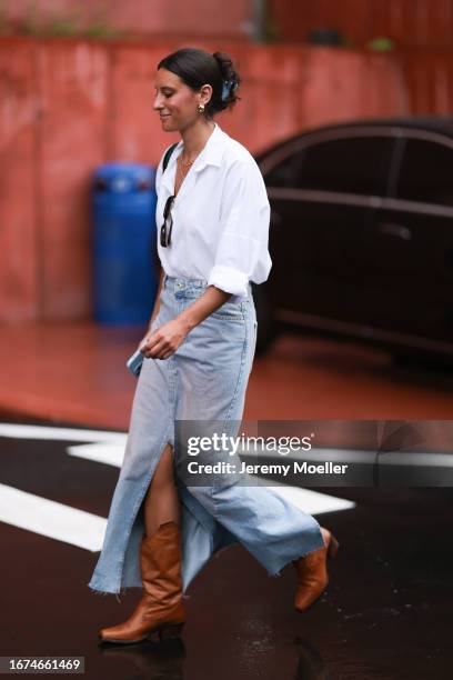 Ulla Johnson Fashion week guest is seen wearing brown leather boots, a wide denim jeans skirt, a white shirt and black shades on September 10, 2023...