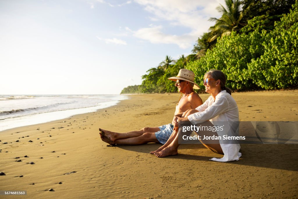 A senior couple sitting on a beach and watching sunset.