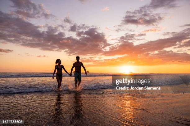 a couple walking out of the ocean at sunset. - goud strand stockfoto's en -beelden