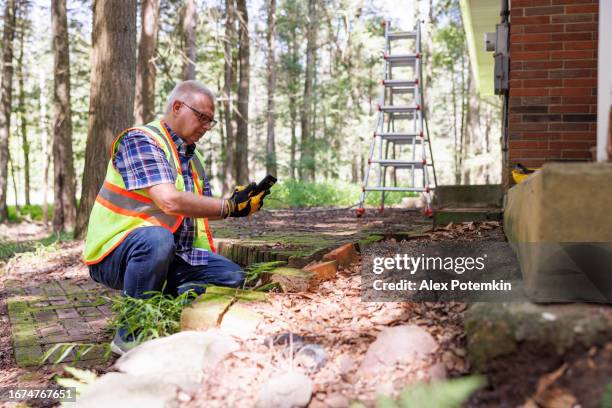 insurance inspector photographing damaged masonry. mature gray haired agent checking consequences on stone steps in house yard after storm - rebuilding stock pictures, royalty-free photos & images