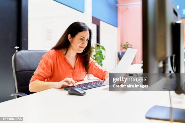 woman with brown hair working in a modern office, entering monthly report data into the system. - dedicación fotografías e imágenes de stock