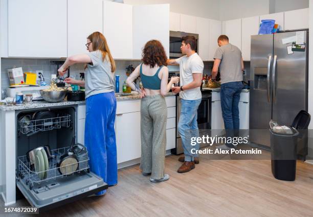 multiracial family cooking and washing dishes together, stand by kitchen counter. young couple and their parents, ready for party, do household chores in the kitchen. rearview - husband cleaning stock pictures, royalty-free photos & images