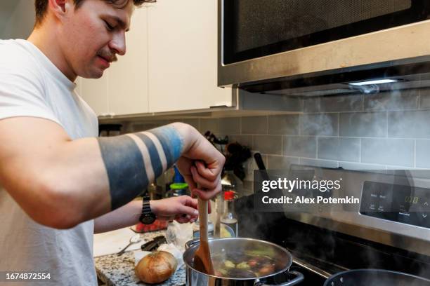 taste of home: hispanic man with mustache and navy officer tattoo stirring vegetable broth in steamy kitchen - boiled potato imagens e fotografias de stock