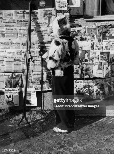 Olympic Winter Games in 1936 in Garmisch-Partenkirchen. A woman in a fur jacket looks at various newspapers at a kiosk. Germany. Photograph. 1936....