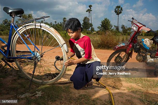 Phan Champa, whose mother says she is seven, fills bike and moto tires will air in front of her family’s house. She is also in charge of caring for...