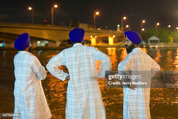 Trio of Sikh men wait for a river taxi at Phra Pok Klao bridge at night along the Chao Phraya River..