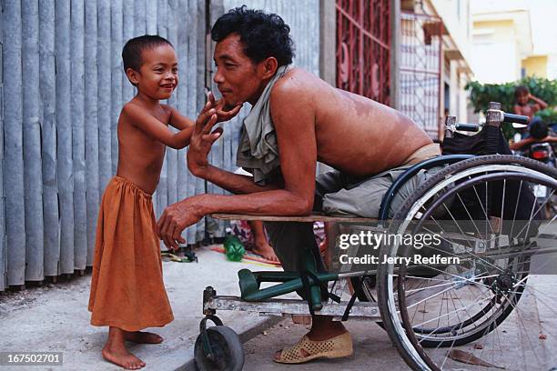 Nhat Pon plays with his older daughter in the shade of Wat Ounalom. He lost his leg while a soldier, and now makes a poor living as a beggar. He...