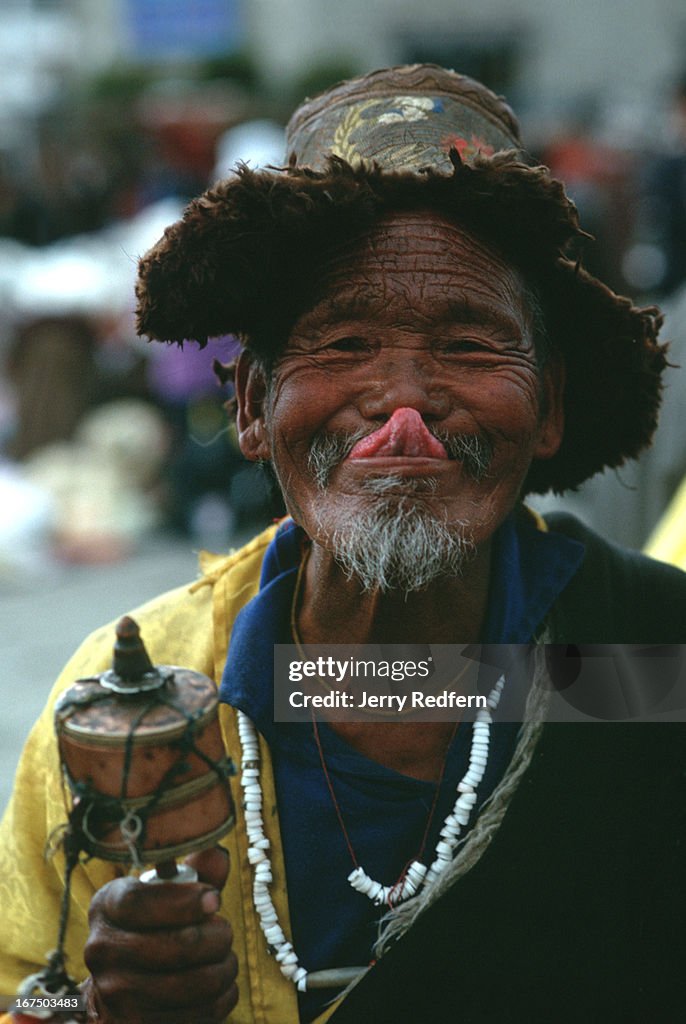 A Tibetan Buddhist touches his nose with the tip of his...