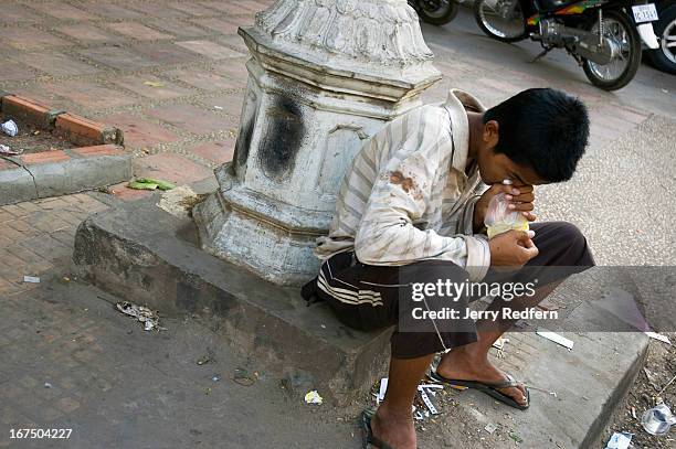 Teenage boy sniffs a bag of glue along a busy street in the middle of the capital. Homeless boys around the country often sniff glue for two reasons:...