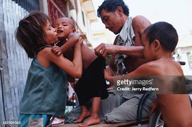 Nhat Pon with the help of his older daughter and another homeless child, checks the pants of his young daughter in the shade of Wat Ounalom. He lost...
