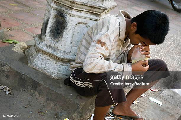 Teenage boy sniffs a bag of glue along a busy street in the middle of the capital. Homeless boys around the country often sniff glue for two reasons:...