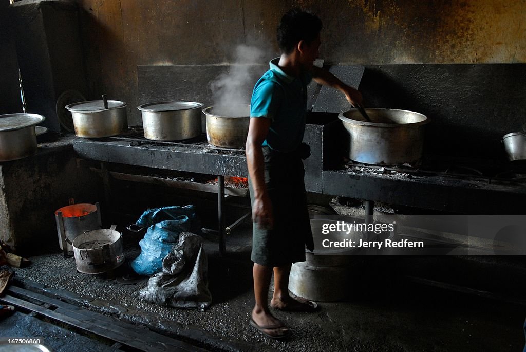 A teenage boy stirs a pot of curry in the kitchen of a...