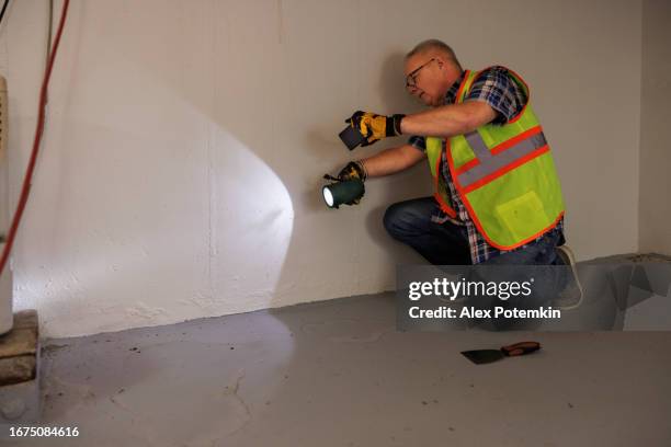 agente de reclamos maduro tomando fotos de derrames en las paredes y el piso del sótano. rastros de derrame en el piso debido a daños por agua. - flooded basement fotografías e imágenes de stock