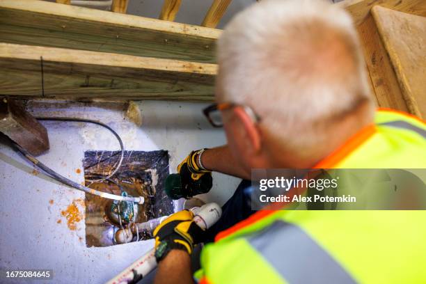 claim agent inspection of sump pit. mature gray haired claim agent in vest inspecting drainage system in basement. above view, focus on sump pump - spoil system stock pictures, royalty-free photos & images