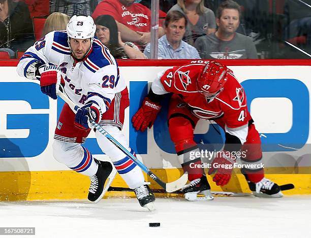 Ryane Clowe of the New York Rangers passes the puck as Marc-Andre Bergeron of the Carolina Hurricanes reaches to pick his stick off the ice during...