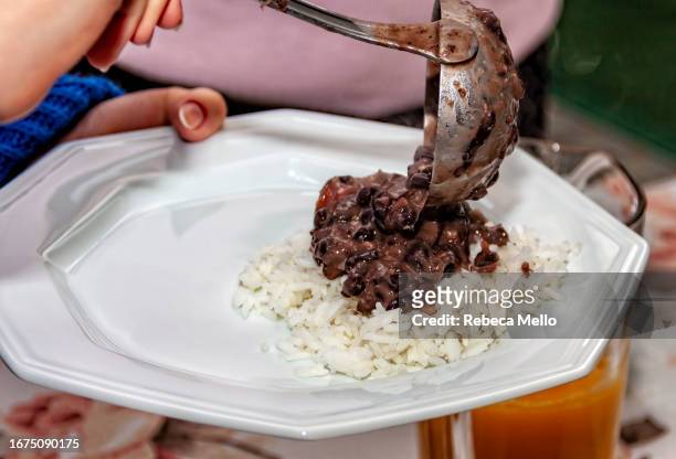 serving pork stew and black beans, brazilian feijoada, over a portion of white rice, using a ladle. - brazilian feijoada dish stock-fotos und bilder