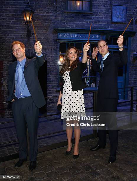 Prince Harry, Catherine, Duchess of Cambridge and Prince William, Duke of Cambridge raise their wands on the set used to depict Diagon Alley in the...