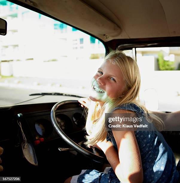 young girl laughing beheind the wheel of old car - girl driving stock-fotos und bilder