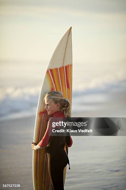 Girl standing on beach with surf board smiling