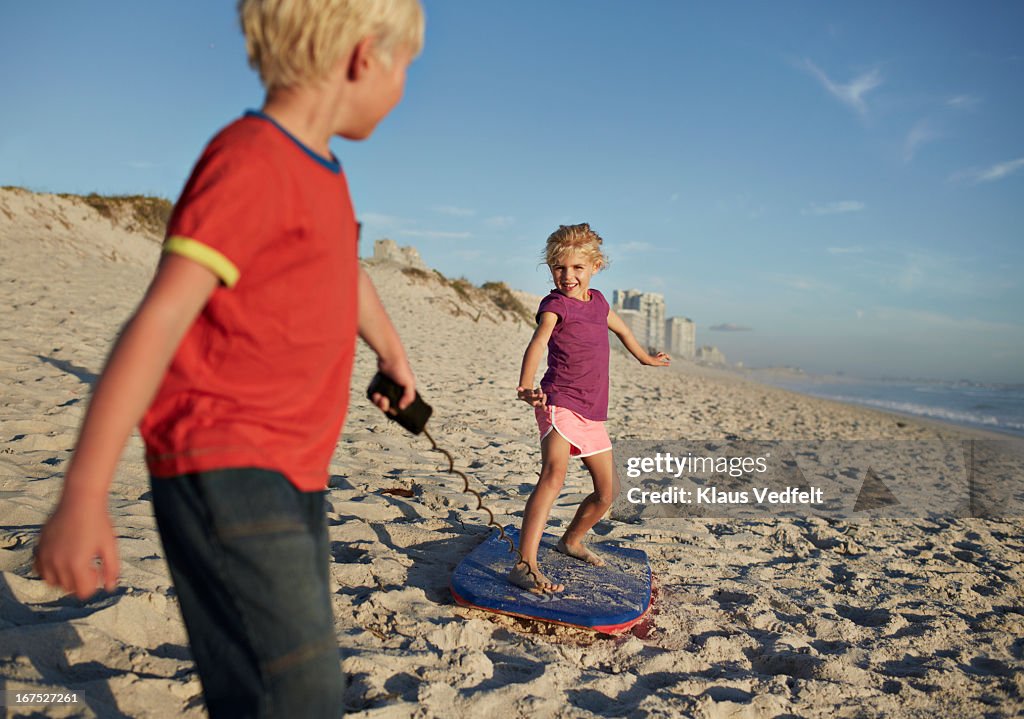 Boy pulling girl on bodyboard on beach