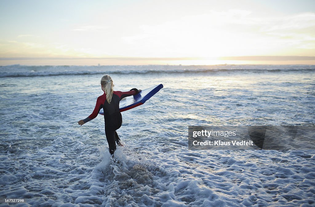 Girl running out in the ocean with bodyboard