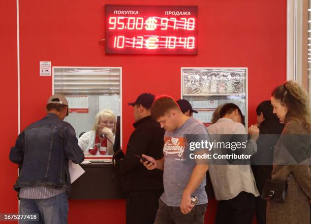 People stand in line at a currency exchange office next to a board showing dollar, euro and ruble exchange rates on September 18, 2023 in Moscow,...