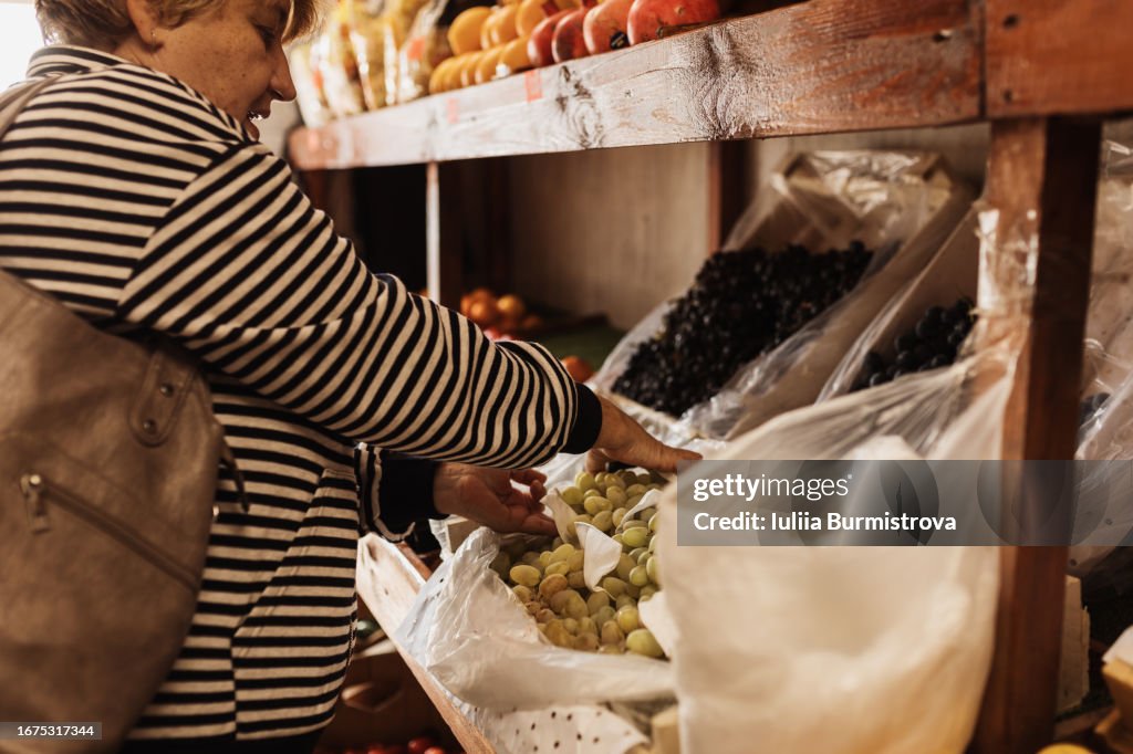 Concentrated woman standing near containers full of juicy grape, choosing bunch of fruits and preparing to pick fresh crops.
