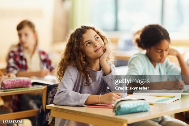 colegiala sonriente soñando despierto en una clase en la escuela primaria. - niña en edad escolar fotografías e imágenes de stock