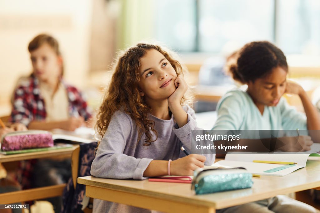 Smiling schoolgirl day dreaming on a class at elementary school.
