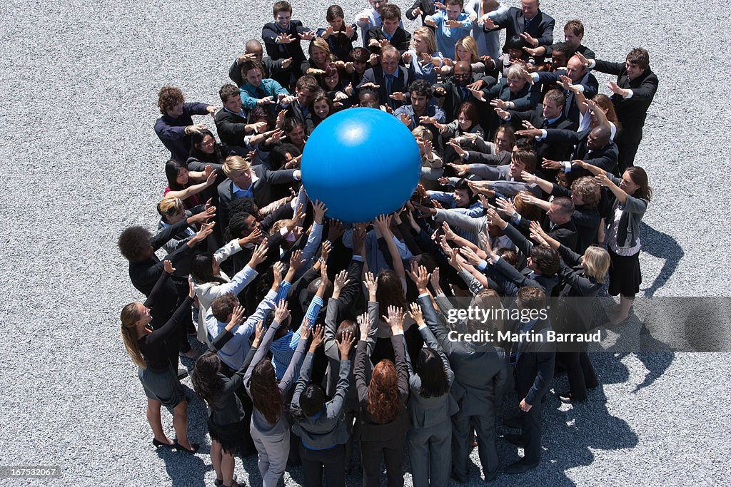 Crowd of business people in huddle reaching for globe