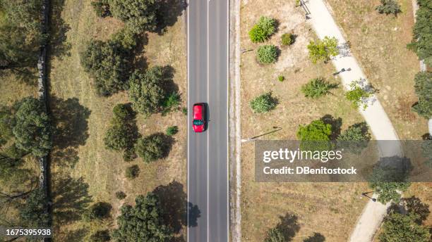 aerial drone view of a road with vegetation on the sides and a red car driving through it. concept of traffic, highway, travel, circulation, roads, driving and helicopter view. - coche carretera fotografías e imágenes de stock