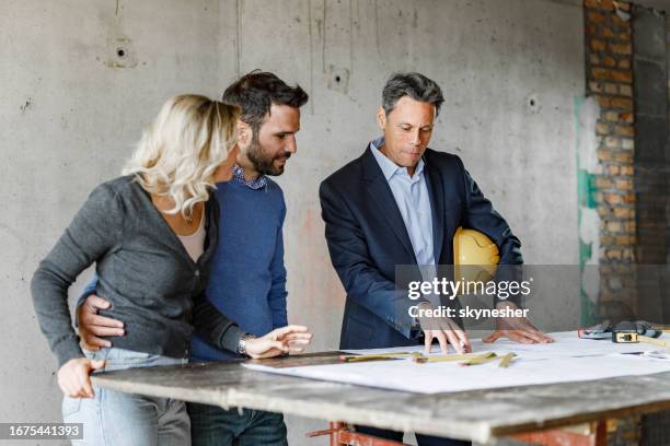 young couple and their architect examining blueprints at construction site. - architect stockfoto's en -beelden