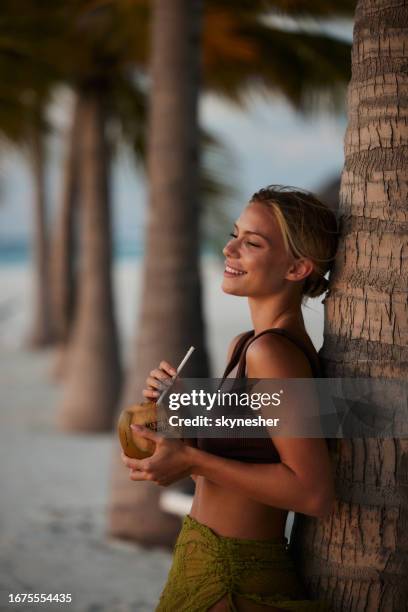 happy woman enjoying in coconut drink on the beach. - coconut beach woman stock pictures, royalty-free photos & images