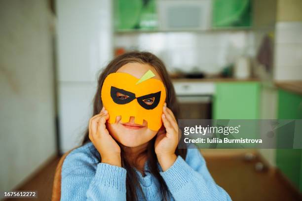 talented girl tries on handcrafted halloween mask made from orange felt - homemade mask stock pictures, royalty-free photos & images