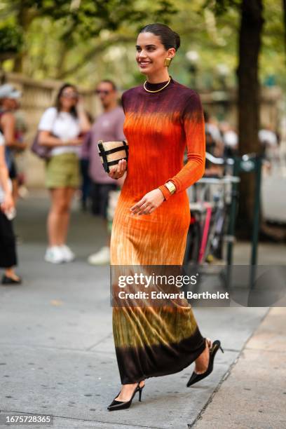 Sara Sampaio wears a necklace, golden earrings, a purple and orange colored dress, a bag, black high heel pointed shoes / pumps, outside Altuzarra,...