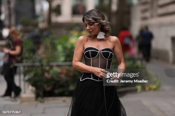 Olga Ferrara is seen wearing white cotton flower neck detail, a see through black Munique corset with white stitching, a black ruffled JNBY midi...