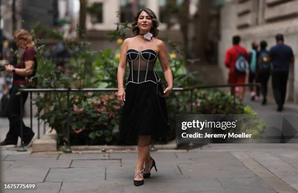 Olga Ferrara is seen wearing white cotton flower neck detail, a see through black Munique corset with white stitching, a black ruffled JNBY midi...