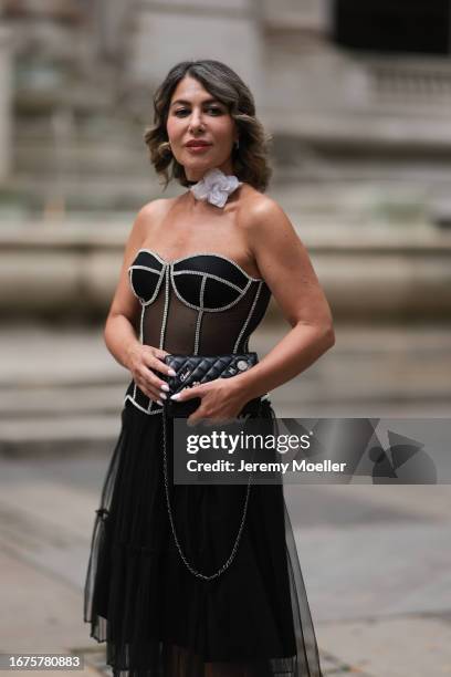 Olga Ferrara is seen wearing white cotton flower neck detail, a see through black Munique corset with white stitching, a black ruffled JNBY midi...