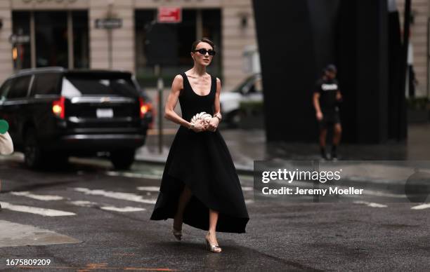 Mary Leest is seen wearing black sunglasses, golden earrings, a black sleeveless midi dress from Jason Wu, golden bracelets, a golden clutch in shell...