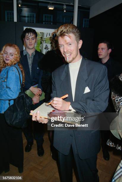 English singer David Bowie signs a cover of 'Aladdin Sane' for a fan at his first solo art exhibition 'New Afro-Pagan and Work 1975-1995' at The...