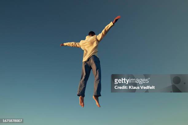 rear view of young man jumping high with arms outstretched - tumbling gymnastics stock pictures, royalty-free photos & images