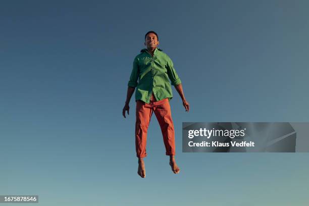 happy man levitating against clear blue sky - mann freudensprung sonne vorderansicht leger stock-fotos und bilder