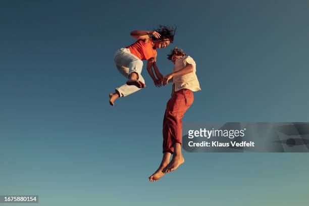 cheerful friends jumping high up in mid-air - mann lachen blick in die kamera stock-fotos und bilder