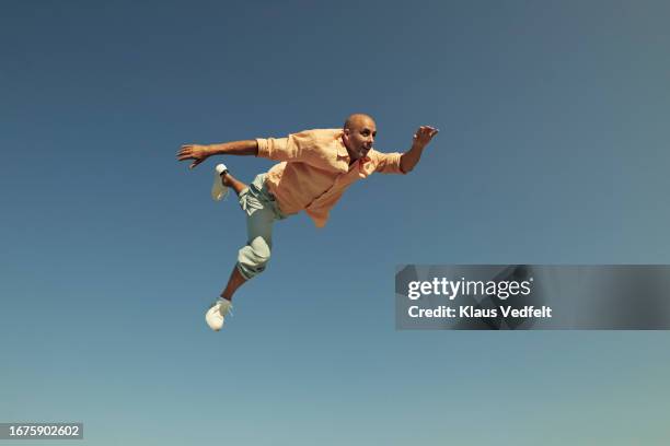 carefree man jumping high in mid-air against blue sky - en medio del aire fotografías e imágenes de stock