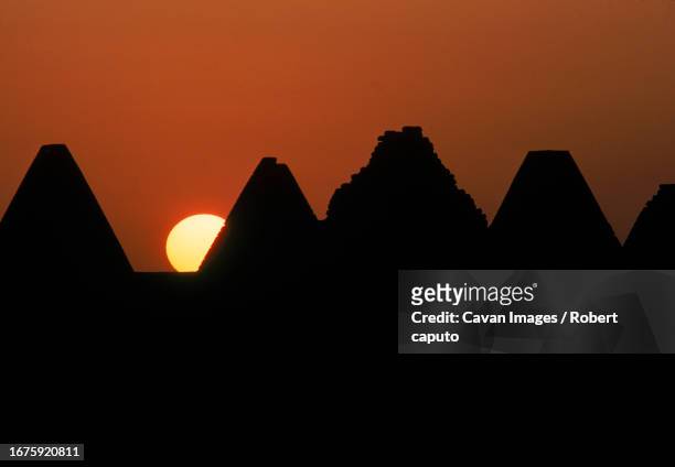 the sun sets behind and silhouettes ancient pyramids, northern sudan - meroe stock-fotos und bilder