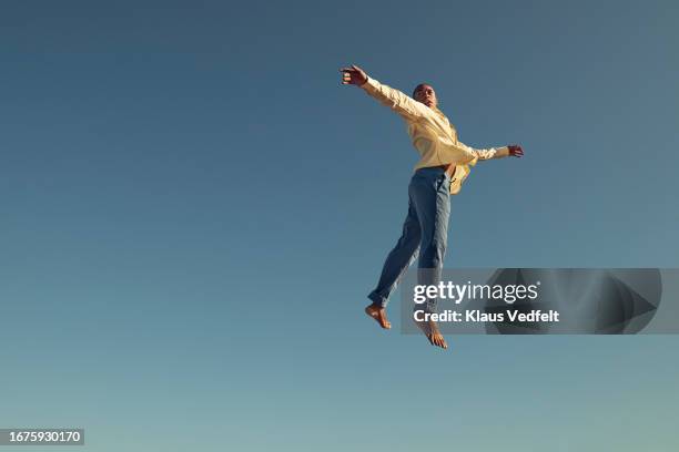 young man jumping with arms outstretched - odds stock-fotos und bilder