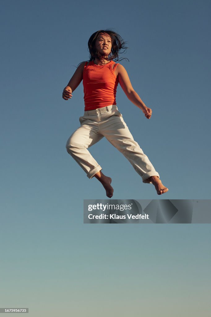 Young woman with tousled hair levitating against blue sky
