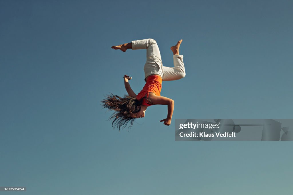 Side view of young woman doing acrobat against clear blue sky