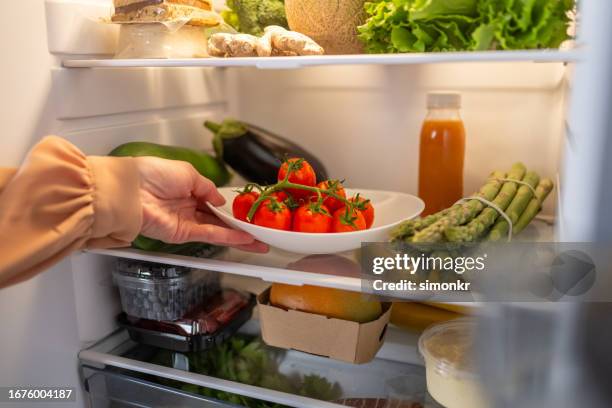 woman hands taking tomato out of refrigerator - koelkast stockfoto's en -beelden