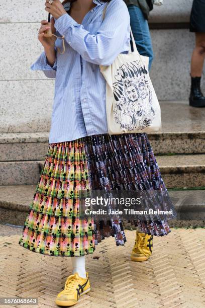 Blue striped shirt, cavas printed tote bag, pleated printed skirt, yellow sneakers, white socks outside the Sandy Liang show during New York Fashion...